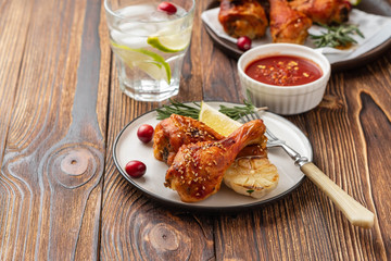 Tasty appetizing baked chicken legs served with spices, rosemary and cranberries on wooden background table. Christmas dish. Copy space.