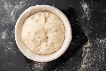 Baking bread. Dough in proofing basket on table with flour, sunflower seeds. Top view.