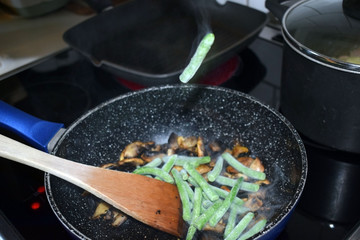 Fried champignons and green beans in a pan. Cooking process. Selective focus.