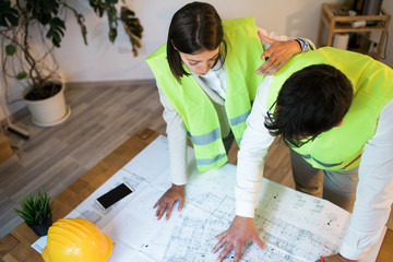 Top view of a team of two young designers working together on a building plan in the office and a business model for the architects project.