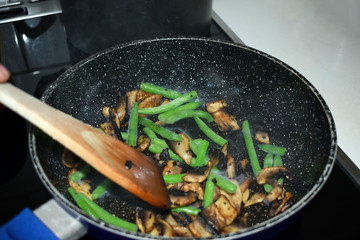 Fried champignons and green beans in a pan. Cooking process. Selective focus.