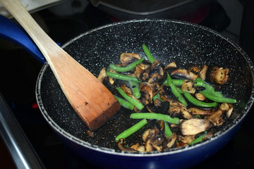Fried champignons and green beans in a pan. Cooking process. Selective focus.
