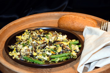 Fried champignons, green beans and eggs on the served table. Ready meal on a wooden dish. Black background. Selective focus.