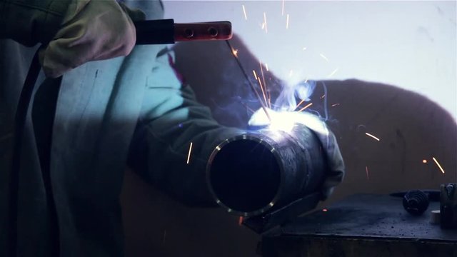welder welds two pieces of steel pipe using electric welding in production