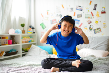 Young asian boy is smiling and listening to music on bedroom