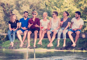 friends enjoying watermelon while sitting on the wooden bridge