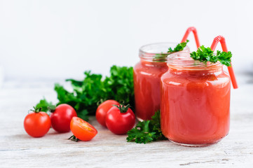 tomato juice in glass jars with cherry tomatoes on a wooden table