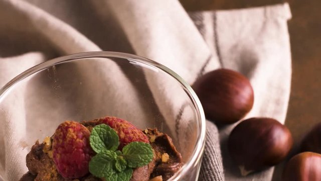 Couple of glasses of chocolate and chestnuts mousse with roasted almods and oats decorated with raspberries and mint leaves.