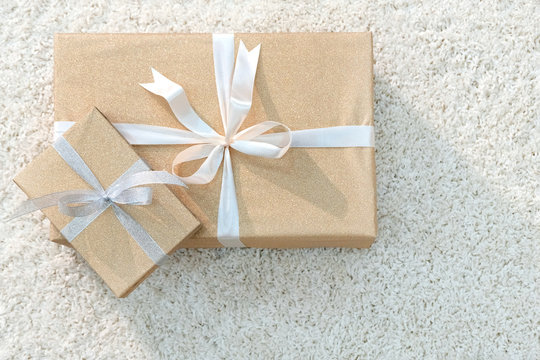 Two boxes with gifts wrapped with golden paper and tied with white ribbon. Soft white carpet. Side light. Copy space.