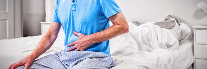 Senior man having stomach pain while sitting on bed