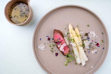 Modern Style classic white asparagus with barbecue dry aged sliced beef fillet and parmesan served as top view on a minimalistic design plate – isolated