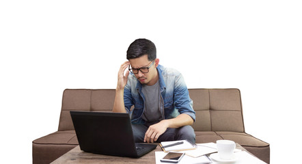 Asian guy looking at laptop with stressful face sitting on sofa working as freelance at home with...