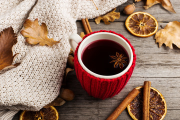 Mulled wine in a cup in a case. Leaves, knitted plaid, dry orange, cinnamon and acorns on the old wooden table, copy space, autumn.