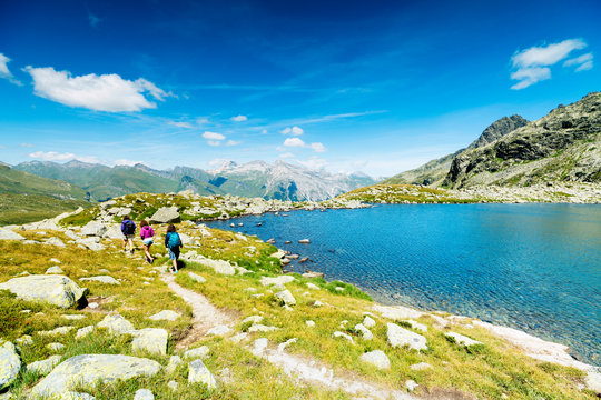 Hikers on footpath on the shore of lake Bergsee, Spluga Pass, canton of Graubunden