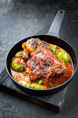 Traditional barbecue leg of lamb with lemon and tomatoes as closeup in a cast-iron skillet