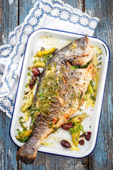 Frisch gegrillte griechische Dorade mit Peperoni und Kalamata Oliven als Draufsicht in einer weißen Bratreine