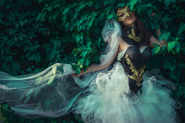 Golden, mysterious woman dressed in white with mask of leaves in copper and gold color in a garden...