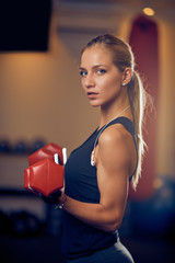 Woman lifting dumbbells and looking at camera. Side view. Healthy lifestyle concept.
