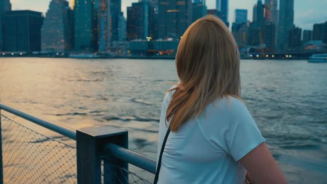 Attractive Caucasian female tourist enjoys the view of New York City Manhattan downtown skyline. 4K UHD