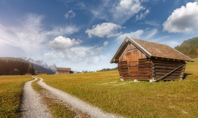 Awesome Autumn Landscape in Bavarian Alps. Alpine summer landscape in the alps with mountains and wooden hut. dirt  road on valley and Sky with clouds on background. Creative collage. Amazing nature