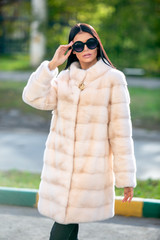 Beautiful brunette in sunglasses and a light fur coat walking down the street