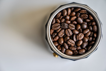 Coffee beans in mocha pot right of center from high angle with white background