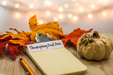 Thanksgiving Food Drive list concept on blank clipboard surrounded with bright leaves and decorative items soft background