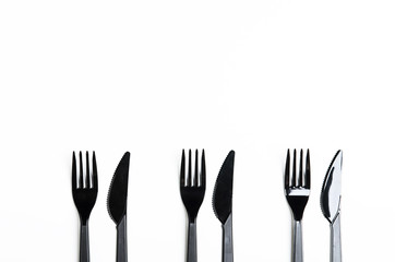 Clean plastic black forks and knives on white background. Disposable dishes, environmental pollution. Copy space, top view, flat lay.