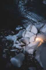 broken icecubes in an ice cave with abstract forms and enlightened by a small light and a waterfall...