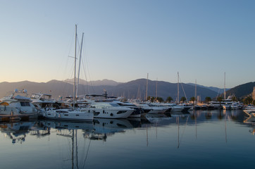 Obraz premium Boats and yachts moored in Adriatic port on background of mountains and sunset.