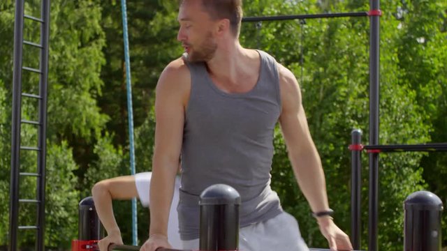Young joyous man and woman in sportswear practicing parallel bars hands walk while training at outdoor gym zone in the park