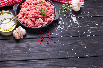Raw minced meat in bowl  with ingredients for cooking on  black table.