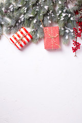 Border from wrapped christmas presents, fur tree branches, red berries on white textured  background.