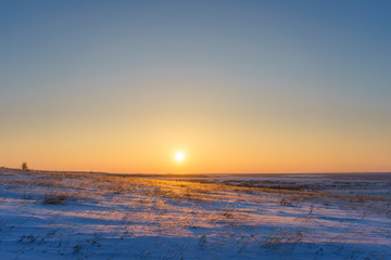 Winter landscape with snow covered plain, blue sky and orange su