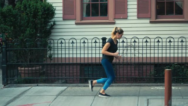 TRACKING Attractive mid-30s Caucasian female putting earphones before evening jog in Downtown NYC Manhattan. 4K UHD