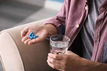Obraz na płótnie Canvas Man holding pills and glass of water, closeup