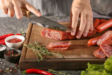 Woman cutting delicious smoked sausage on wooden board