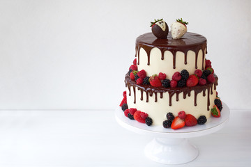 Two-tiered wedding cake in chocolate, with slices strawberries, raspberries, blackberry, decorated with figures of the bride and groom on a white background.