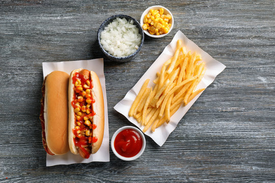 Tasty hot dogs with corn, cut onion and french fries on wooden table - Powered by Adobe