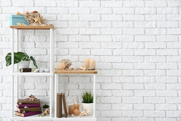 Shelves with books, burning candles, seashells and other decorations near white brick wall