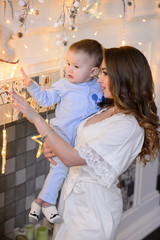 Fototapeta premium Merry Christmas celebration. Beautiful mom and little son at home near the Christmas tree. Christmas miracles.