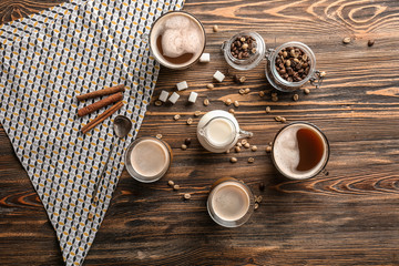 Glasses of tasty aromatic coffee with jug of milk and beans on wooden table