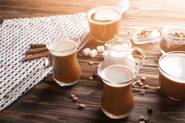 Glasses of tasty aromatic coffee with jug of milk and beans on wooden table