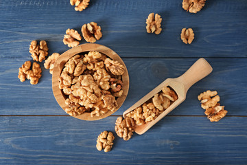 Bowl and scoop with tasty walnuts on color wooden table