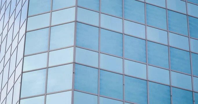 4k time lapse shot with vertical tilt of a glass office building facade reflecting moving clouds.