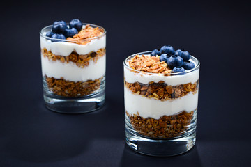 Homemade baked granola with yogurt and blueberries in a glass on a black background. Space for text or design.