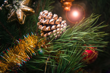 Spruce branch with cone and balls, festive lights on the background.