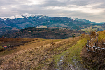 Rural area in november. wooden fence by the country road. mighty ridge with snowy peaks in the distance. gloomy autumn weather