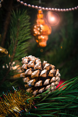 Fototapeta premium Spruce branch with cone and balls, festive lights on the background.