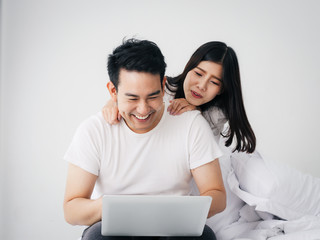 Fototapeta premium Happy Asian couple using laptop on bed together at home, lifestyle concept.